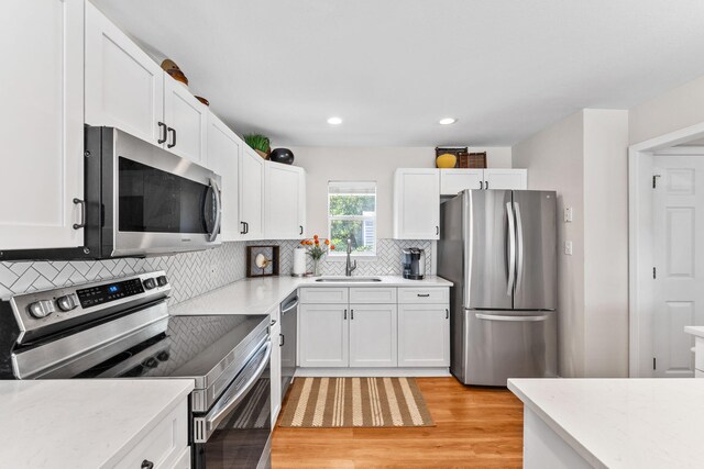 kitchen with light wood-type flooring, tasteful backsplash, stainless steel appliances, sink, and white cabinets