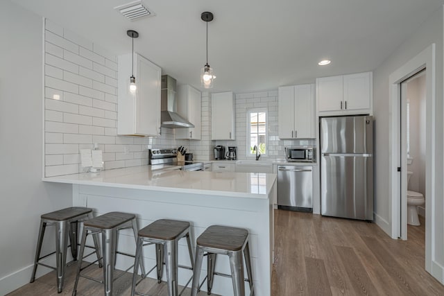 kitchen featuring white cabinets, wall chimney range hood, appliances with stainless steel finishes, and tasteful backsplash