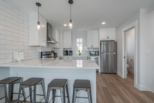 kitchen featuring white cabinets, appliances with stainless steel finishes, wall chimney exhaust hood, backsplash, and kitchen peninsula