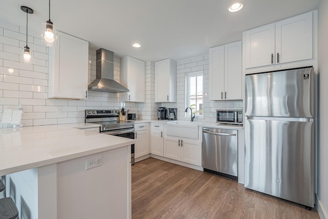 kitchen with appliances with stainless steel finishes, sink, white cabinetry, and wall chimney range hood