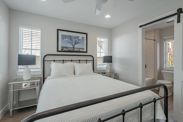 bedroom featuring ceiling fan, a barn door, dark hardwood / wood-style flooring, and multiple windows