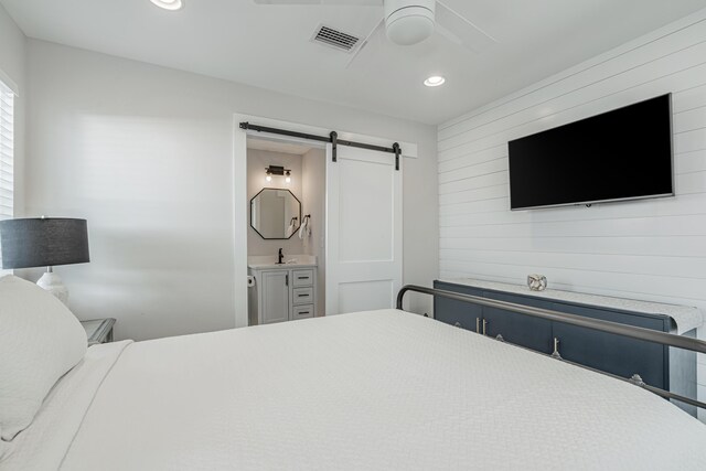 bedroom with ceiling fan, sink, connected bathroom, and a barn door