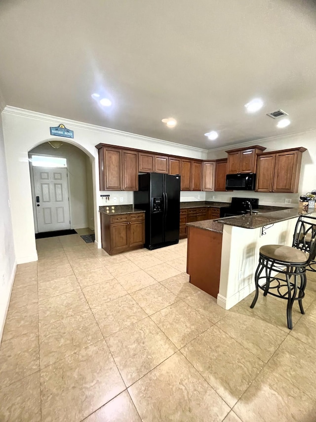 kitchen with a kitchen bar, black appliances, dark stone countertops, light tile patterned flooring, and ornamental molding