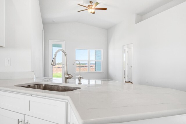 kitchen with white cabinetry, lofted ceiling, sink, ceiling fan, and light stone countertops