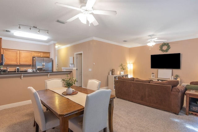 carpeted dining room with rail lighting, ceiling fan, and ornamental molding