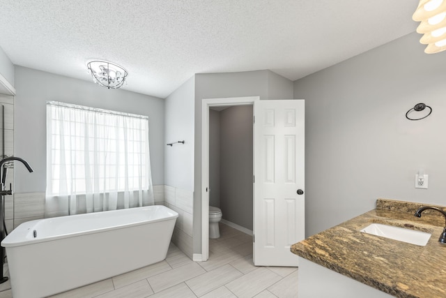 bathroom with toilet, a bathing tub, vanity, a textured ceiling, and tile walls