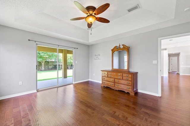 unfurnished room with a textured ceiling, ceiling fan, a tray ceiling, and dark hardwood / wood-style flooring