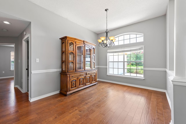 unfurnished dining area featuring dark wood-type flooring, a textured ceiling, and a chandelier