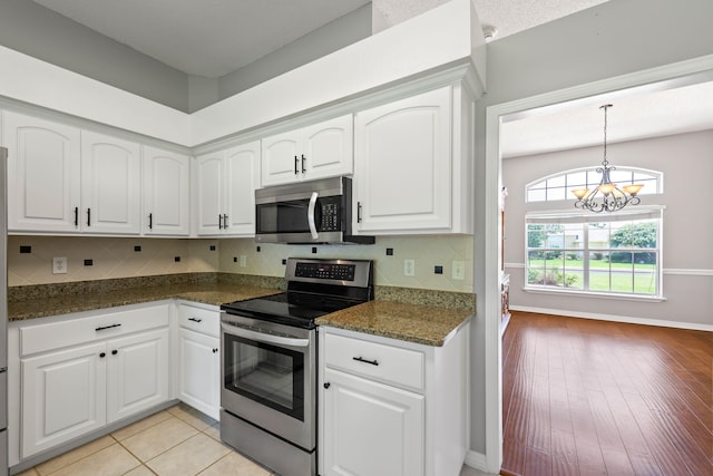 kitchen with dark stone countertops, a notable chandelier, white cabinetry, light hardwood / wood-style flooring, and stainless steel appliances