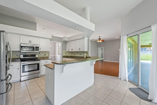 kitchen featuring stainless steel appliances, white cabinetry, ceiling fan, kitchen peninsula, and a breakfast bar area