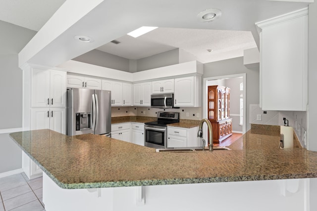 kitchen with dark stone countertops, appliances with stainless steel finishes, kitchen peninsula, and sink