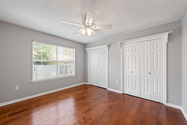 unfurnished bedroom with dark wood-type flooring, a textured ceiling, two closets, and ceiling fan