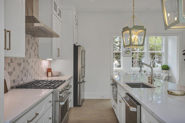 kitchen featuring stainless steel appliances, wall chimney exhaust hood, white cabinetry, and sink