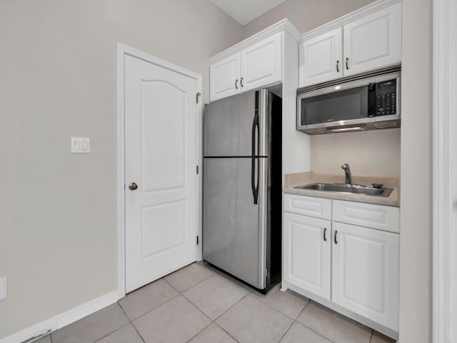 kitchen with appliances with stainless steel finishes, light tile patterned floors, white cabinetry, and sink