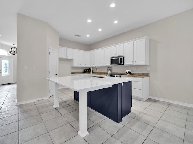 kitchen with sink, an island with sink, light tile patterned flooring, a kitchen bar, and white cabinetry