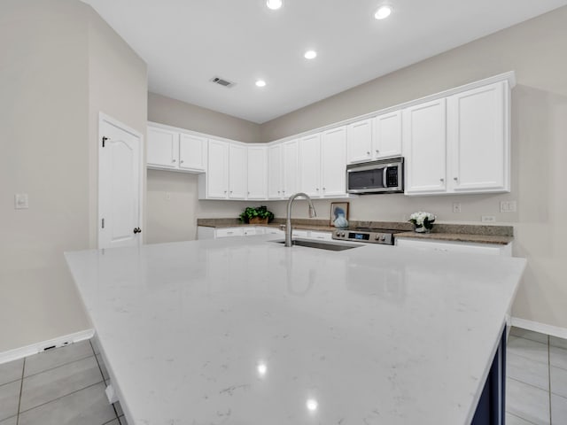 kitchen with white cabinets, a center island with sink, sink, light tile patterned floors, and light stone counters