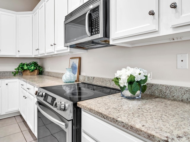 kitchen featuring light tile patterned flooring, light stone countertops, white cabinetry, and appliances with stainless steel finishes