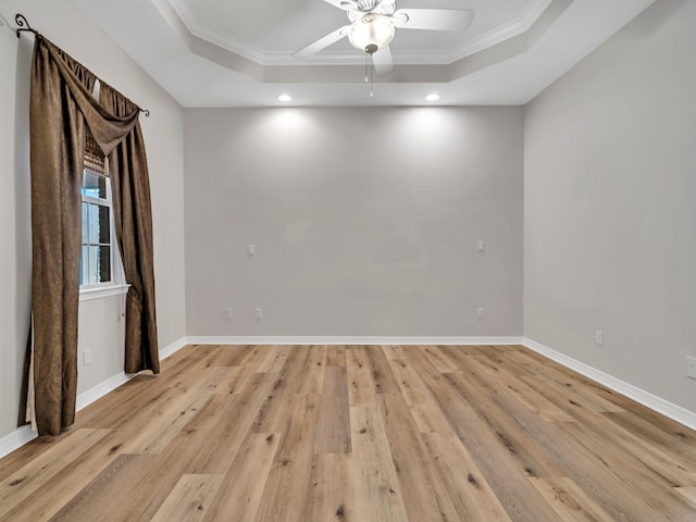 empty room with ceiling fan, light hardwood / wood-style floors, a raised ceiling, and crown molding