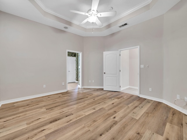 empty room featuring ceiling fan, a high ceiling, a raised ceiling, crown molding, and light hardwood / wood-style floors