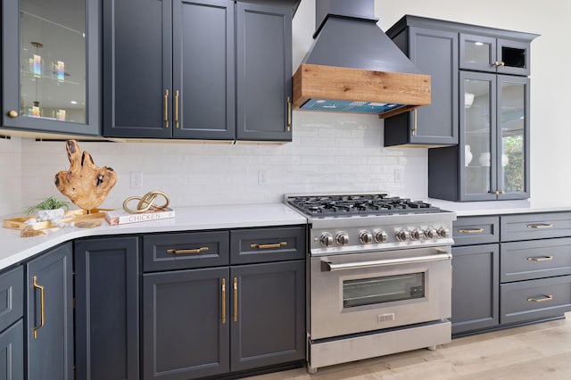 kitchen featuring premium range hood, light countertops, glass insert cabinets, high end stainless steel range oven, and backsplash