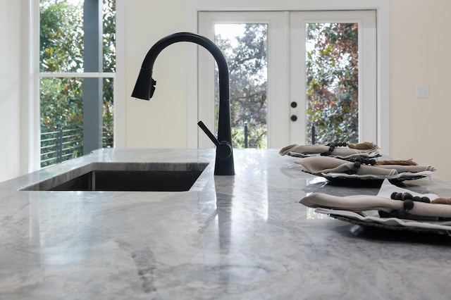 interior details featuring light stone counters, french doors, and a sink