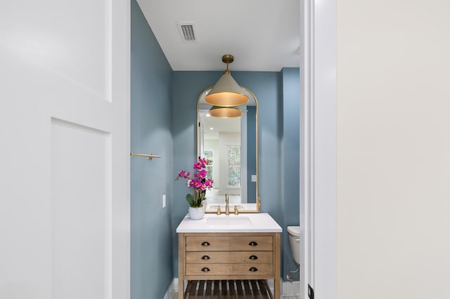 half bath featuring visible vents, baseboards, toilet, and vanity