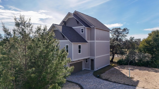 view of property exterior with decorative driveway, a garage, and roof with shingles
