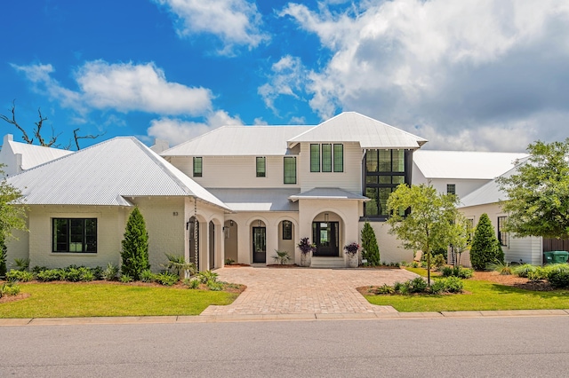 view of front of home featuring brick siding, metal roof, decorative driveway, and a front yard