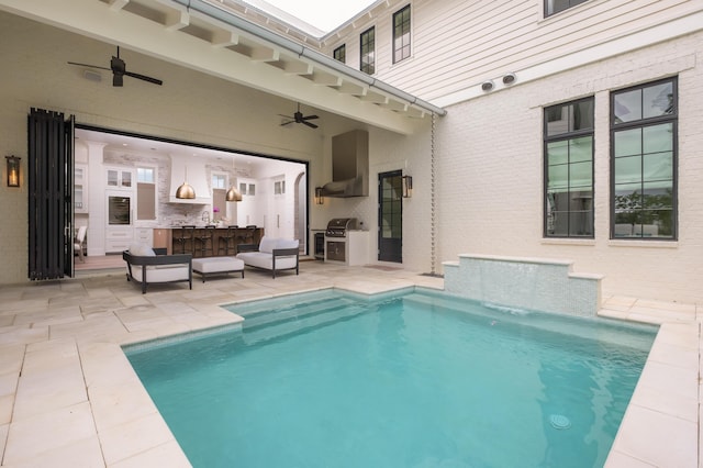 view of pool with ceiling fan, a patio area, outdoor dry bar, and an outdoor kitchen