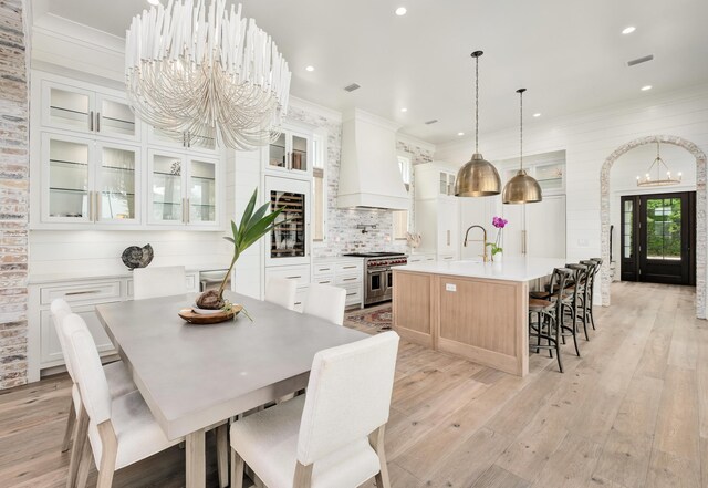 dining room with sink, light wood-type flooring, a notable chandelier, and crown molding