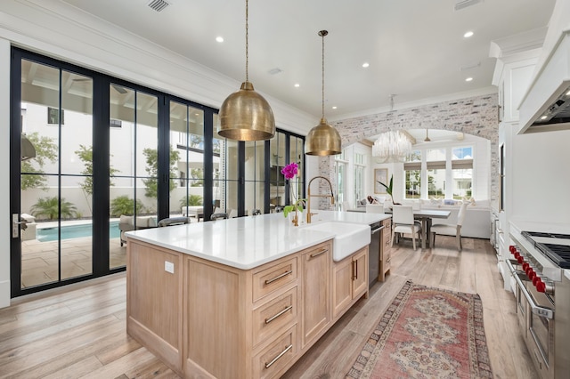 kitchen featuring an island with sink, light brown cabinets, a sink, light wood-style floors, and crown molding