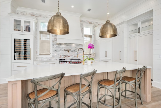 kitchen with custom exhaust hood, light wood-style flooring, light countertops, and ornamental molding