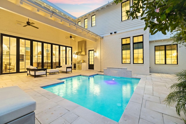 pool at dusk with ceiling fan and a patio area