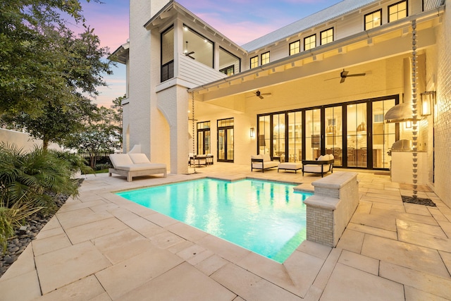 pool at dusk with ceiling fan, an outdoor hangout area, and a patio area