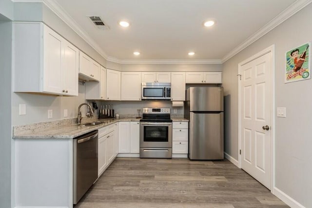 kitchen featuring stainless steel appliances, ornamental molding, white cabinets, a sink, and wood finished floors