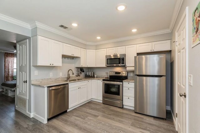 kitchen with visible vents, ornamental molding, stainless steel appliances, white cabinetry, and a sink