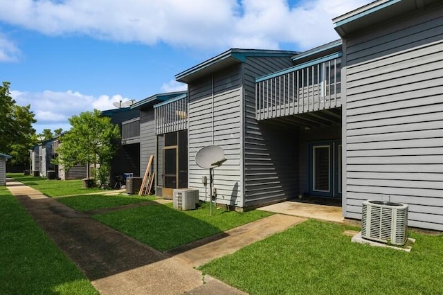 rear view of property featuring a lawn, a balcony, and central air condition unit