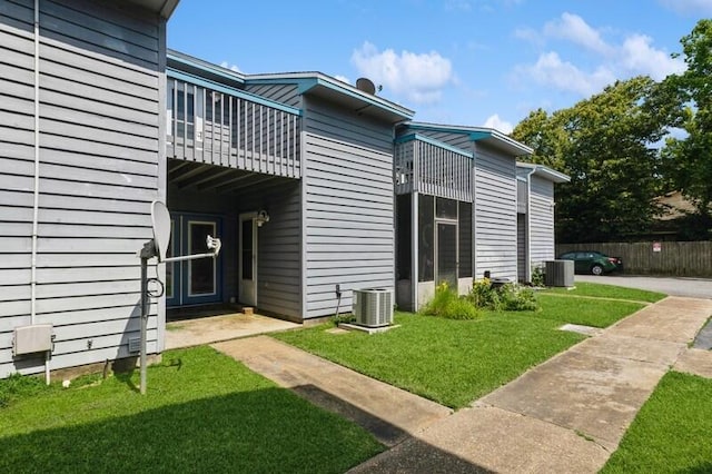 exterior space with fence, a lawn, a balcony, and central air condition unit