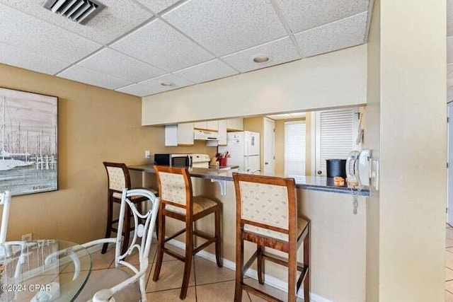 kitchen featuring white cabinets, white refrigerator, a drop ceiling, and light tile patterned floors