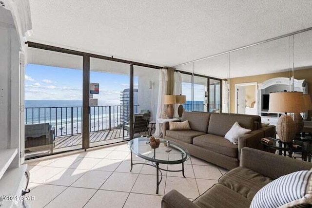 living room featuring a textured ceiling, a wall of windows, light tile patterned floors, and a water view