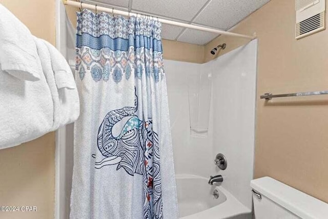 bathroom featuring shower / bath combo, toilet, and a drop ceiling