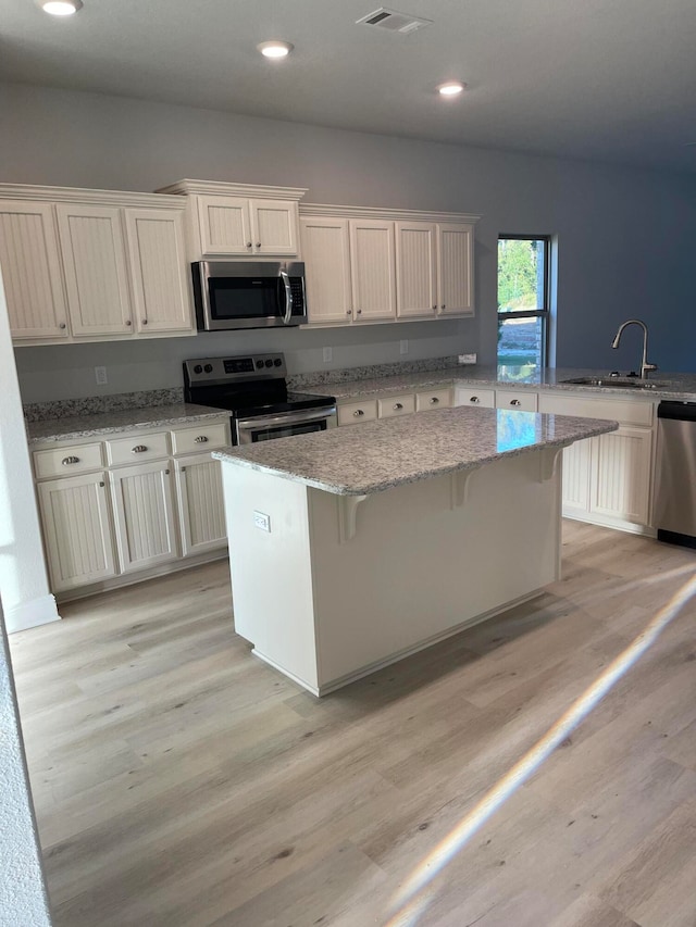 kitchen featuring a breakfast bar, light wood-type flooring, a center island, light stone countertops, and appliances with stainless steel finishes