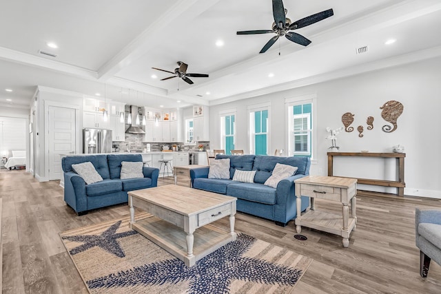 living room featuring ceiling fan, light wood-type flooring, crown molding, and beamed ceiling