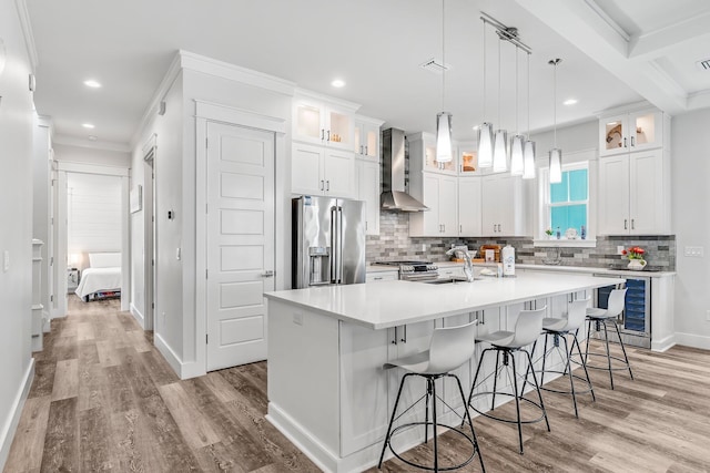 kitchen featuring high end appliances, a center island with sink, wall chimney range hood, beverage cooler, and white cabinetry