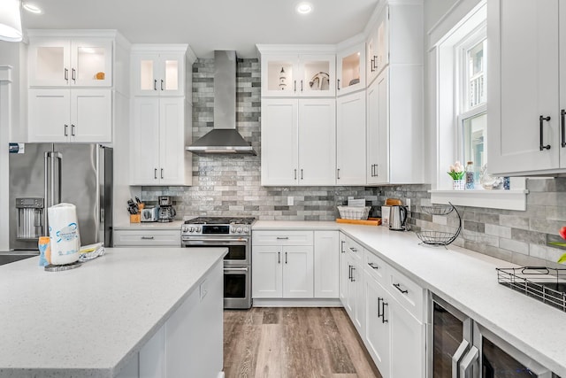 kitchen with appliances with stainless steel finishes, white cabinetry, wall chimney range hood, and decorative backsplash