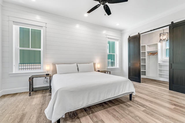 bedroom with ceiling fan, a barn door, crown molding, and hardwood / wood-style floors