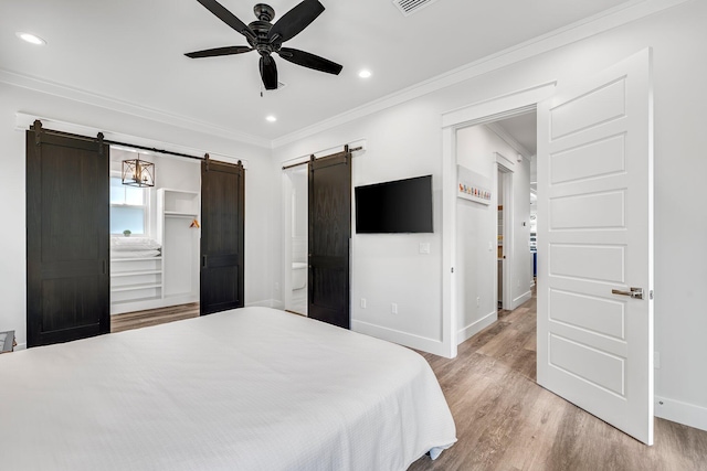 bedroom featuring connected bathroom, a barn door, wood-type flooring, crown molding, and ceiling fan