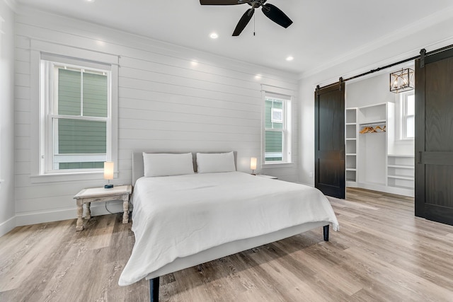 bedroom featuring ornamental molding, light hardwood / wood-style floors, a barn door, a walk in closet, and ceiling fan