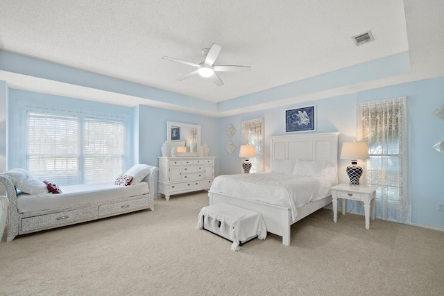 carpeted bedroom featuring ceiling fan, a tray ceiling, and a textured ceiling