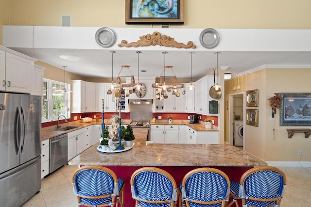 kitchen with sink, appliances with stainless steel finishes, white cabinetry, washer / dryer, and decorative light fixtures